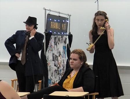 Three students in costumes perform a skit.  Two of them are pretending to talk on telephones.