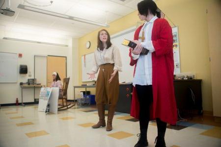 Two students in a classroom perform a skit while wearing costumes.