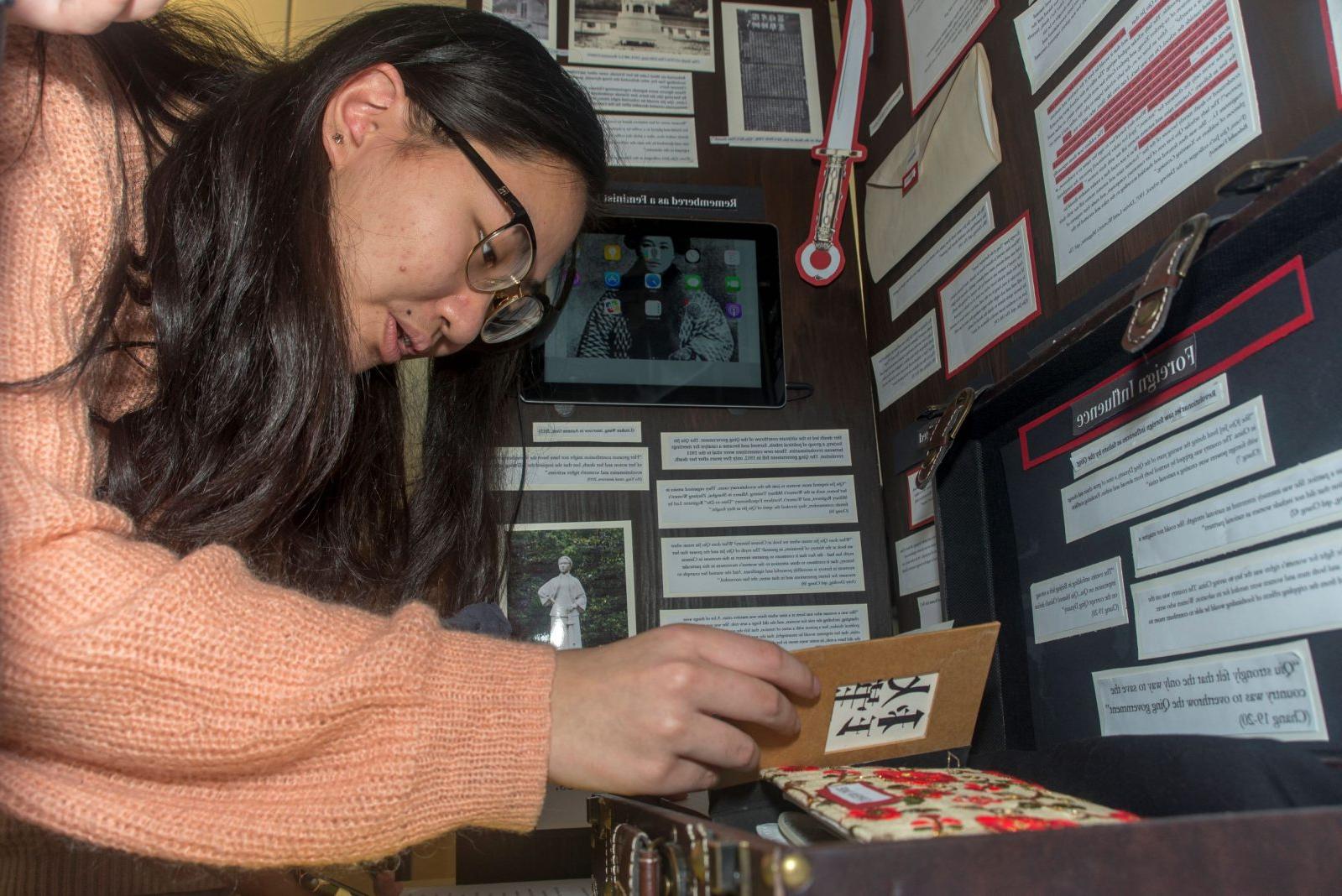 A student opens a booklet to read, which is part of a display at the base of an exhibit board.