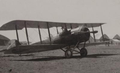 Black and white photograph of two small plane. Several tents and a group of soldiers can be seen in the background.